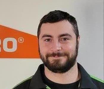 Crew chief, Tyler standing in our office in front of our SERVPRO logo
